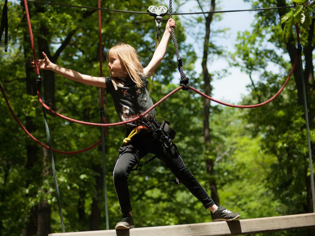 A child navigating ropes in an outdoor adventure park, enjoying the thrill.